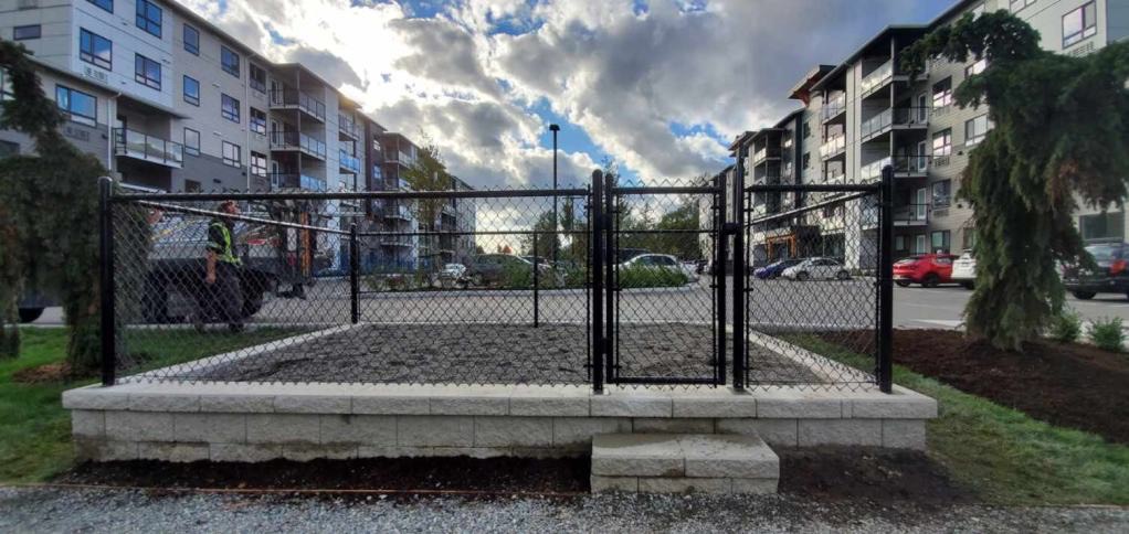 Black vinyl-coated chain link fence enclosing a raised playground area — Coquitlam, BC commercial project.