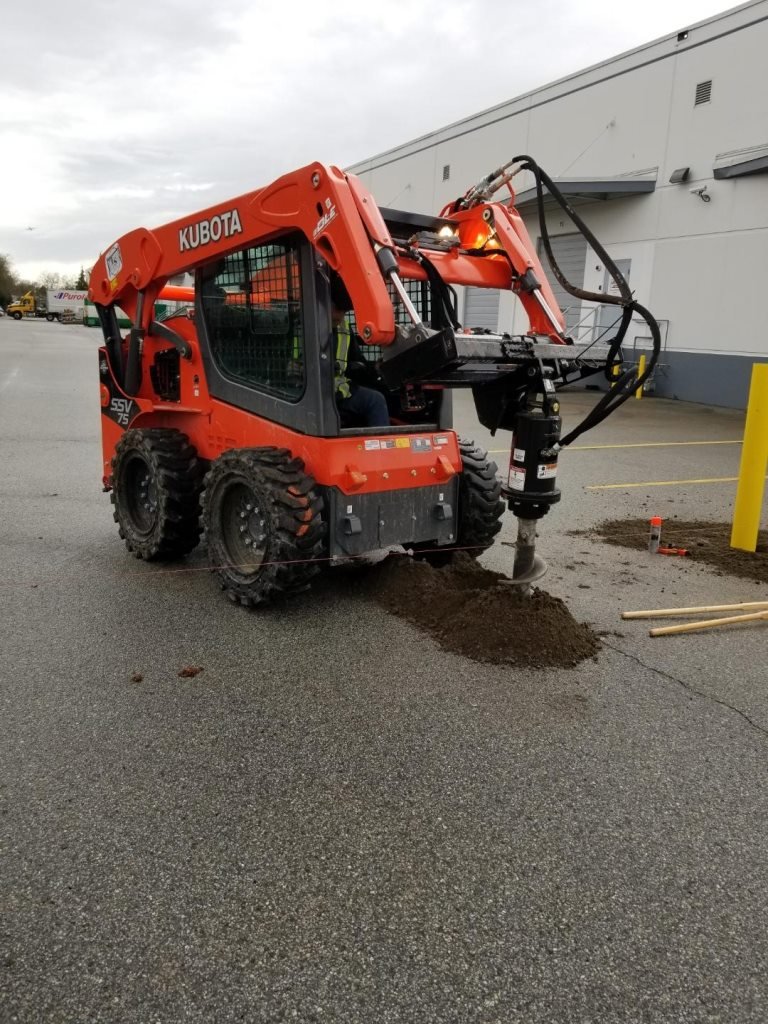 Kubota skid steer with hydraulic auger drilling fence post holes on a commercial lot