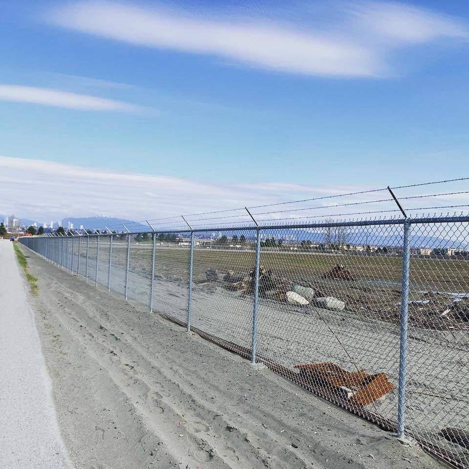 Tall galvanized chain link perimeter fence with three-strand barbed wire — Burnaby, BC commercial project.