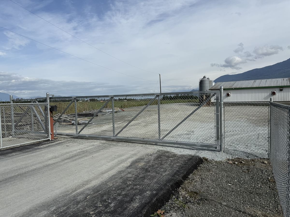 Galvanized cantilever driveway gate securing an industrial farm yard with mountain backdrop — West Vancouver, BC commercial project.