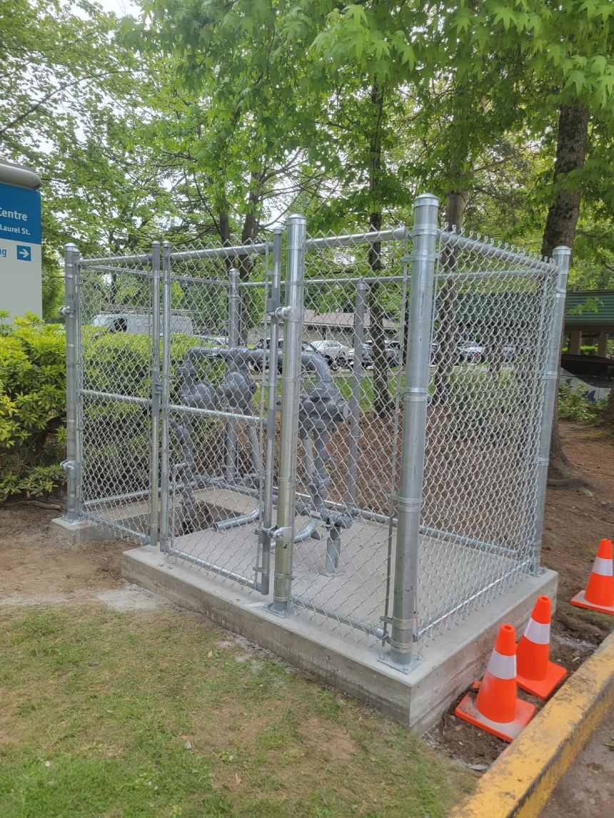 Galvanized chain link security cage protecting utility equipment on a concrete pad — Port Moody, BC commercial project.