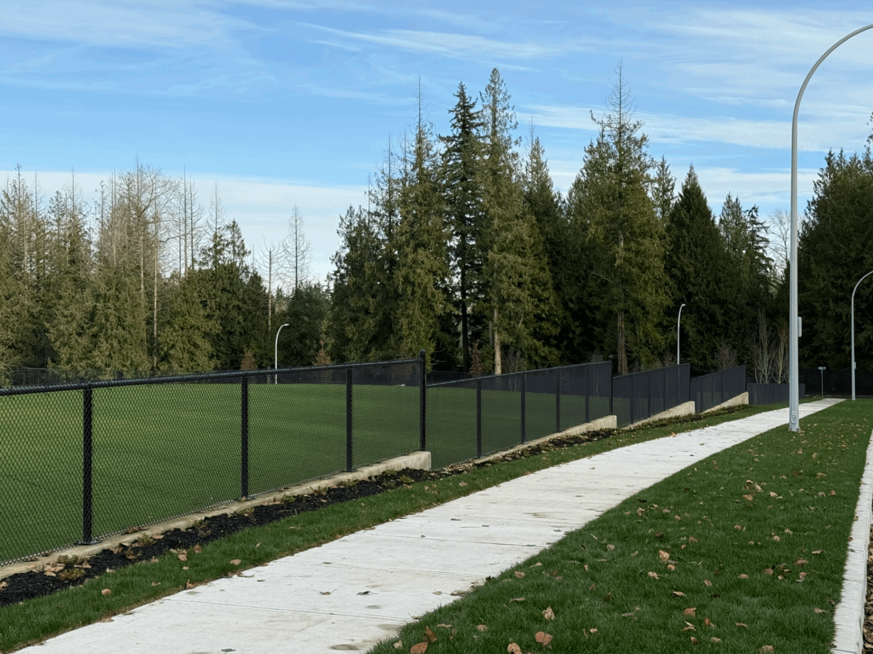 Black vinyl-coated chain link perimeter fence with privacy screening around a turf sports field in Langley BC