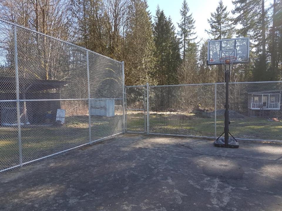 Galvanized commercial-grade chain link perimeter fence with walk-through gate around a private recreational court in the Fraser Valley.