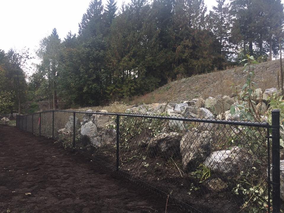 Black chain-link fence along a rock-wall hillside — photograph supplied by LS Fencing & Metal Work